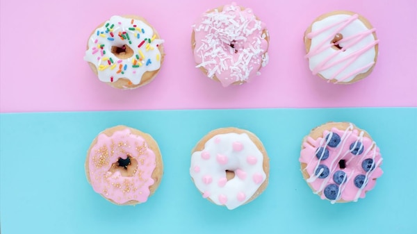 An image of six brightly decorated donuts positioned on a pink and blue background.