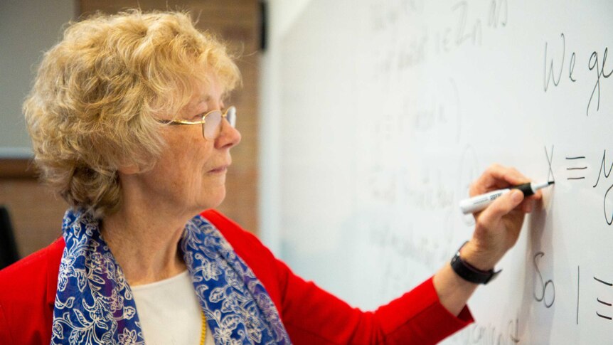 Cheryl Praeger writes formulas on a whiteboard
