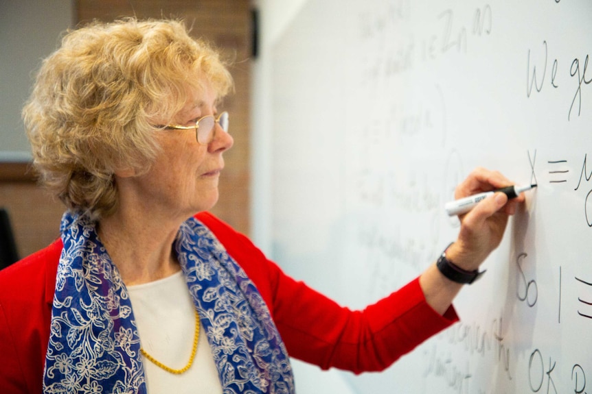 Cheryl Praeger writes formulas on a whiteboard