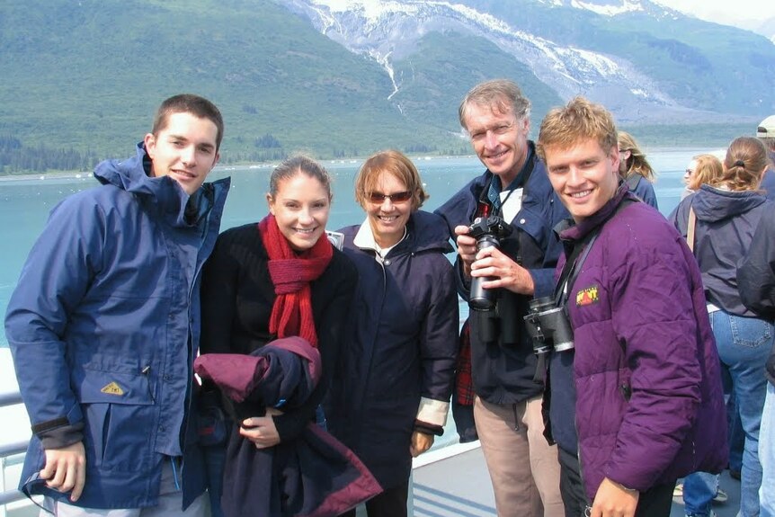 two young men, a young woman and older couple onboard a boat with snow capped mountains in the background