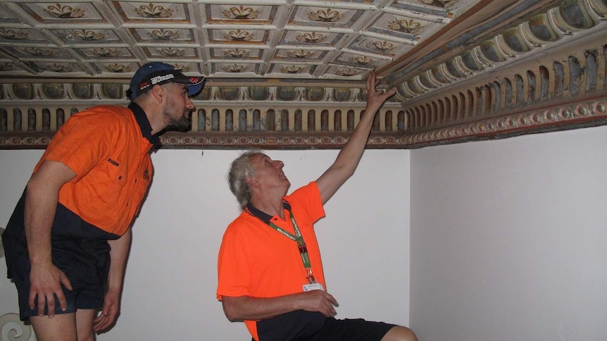 Two men dressed in high-vis shirts look at the pressed-tin ceiling.