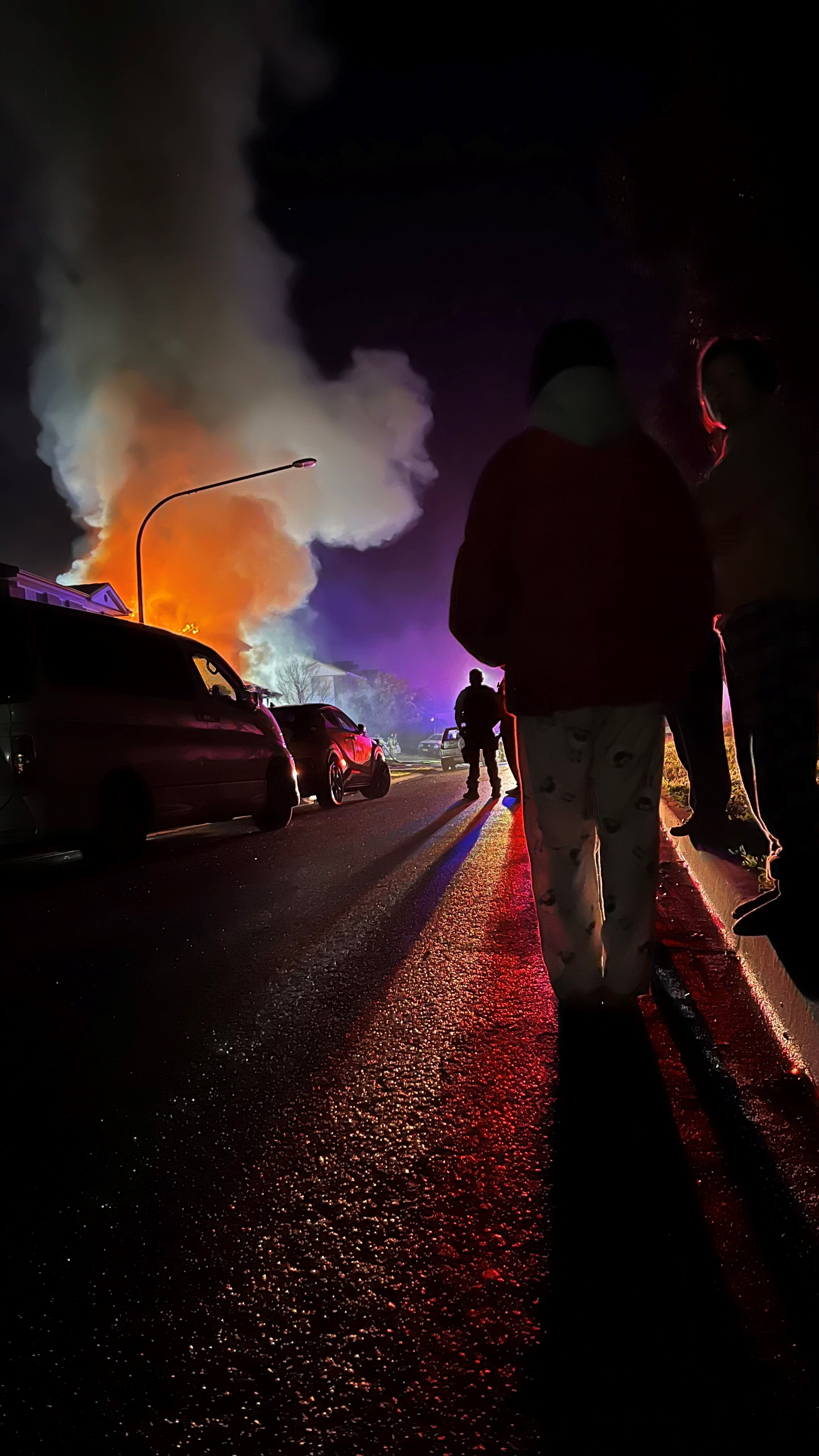 People stand on the street looking at an orange smoke cloud billowing from a house