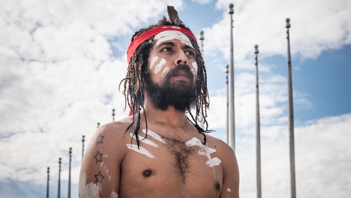 An aboriginal man in traditional dress looking towards the sky
