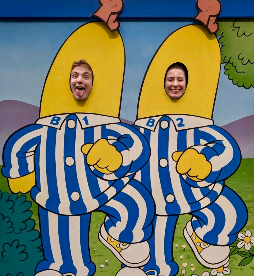 Two people sticking their heads through the holes in a Bananas in Pyjamas mural. One is poking out their tongue.