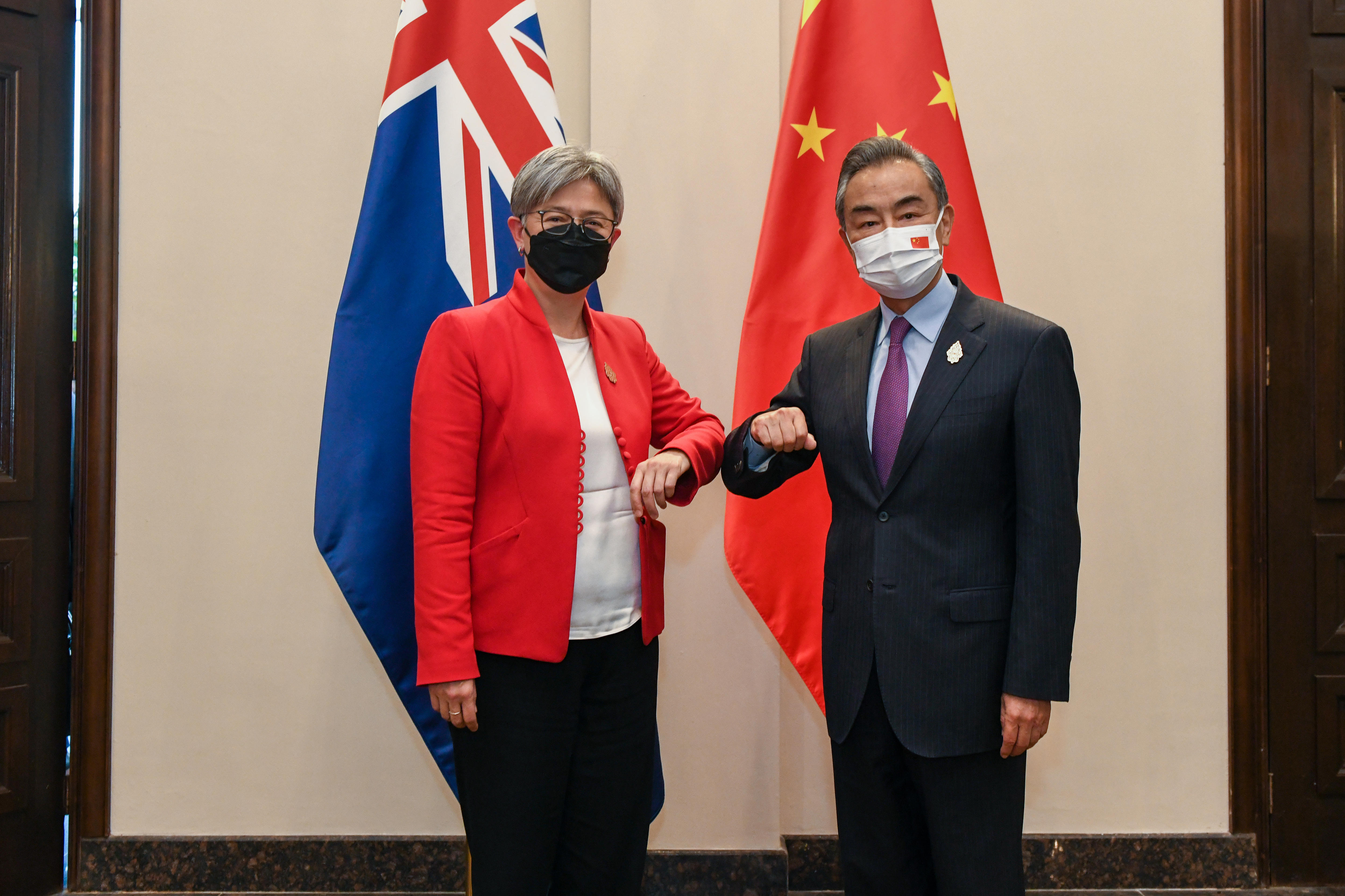 一男一女在镜头前撞肘，身后是澳大利亚和中国的国旗。