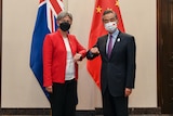 A man and woman bump elbows for the camera with the Australian and Chinese flags behind them.