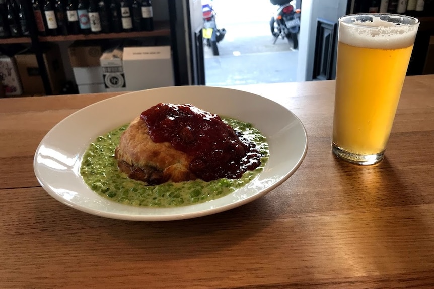 A plate with a pie and mushy peas and a glass of beer