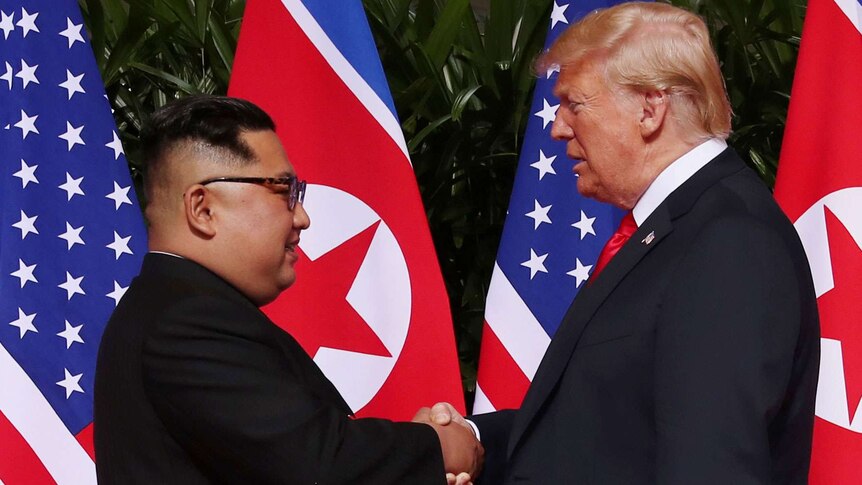 Kim and Trump look each other in the eye as they shake hands.