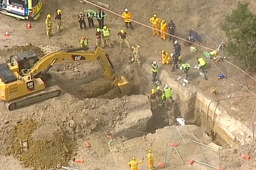 Heavy machinery digs out a collapsed trench as emergency services personnel look on.