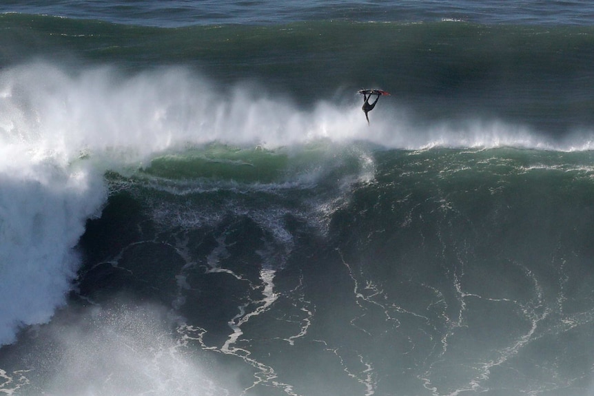 A surfer flies off the top of a big wave, with his board above his head.