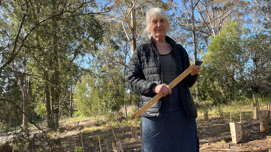 A woman stands in front of bushland.