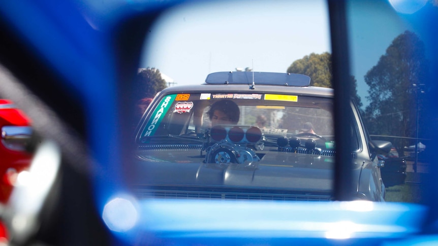 A man is seen through a mirror sitting in his car at the Summernats festival in Canberra.