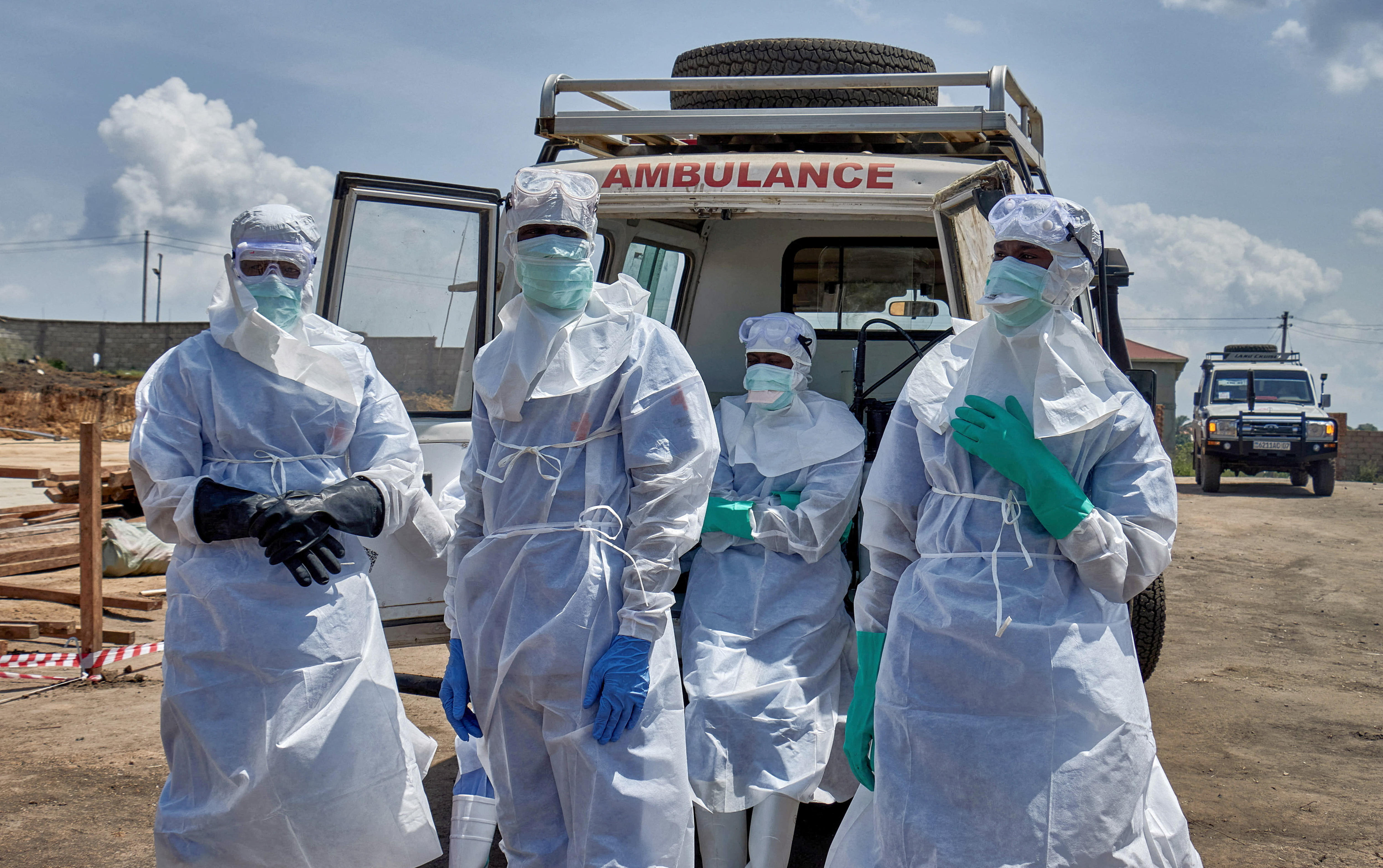 Healthcare workiers in ppe and masks stand in front of an ambulance.