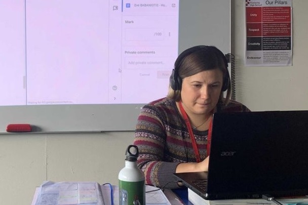 A female teacher sits in front of a screen in an empty classroom.