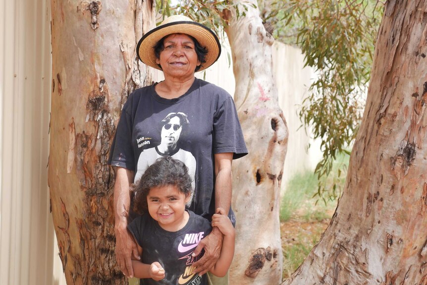 An older Indigenous woman and a young girl stand in front of a tree in Kalgoorlie.