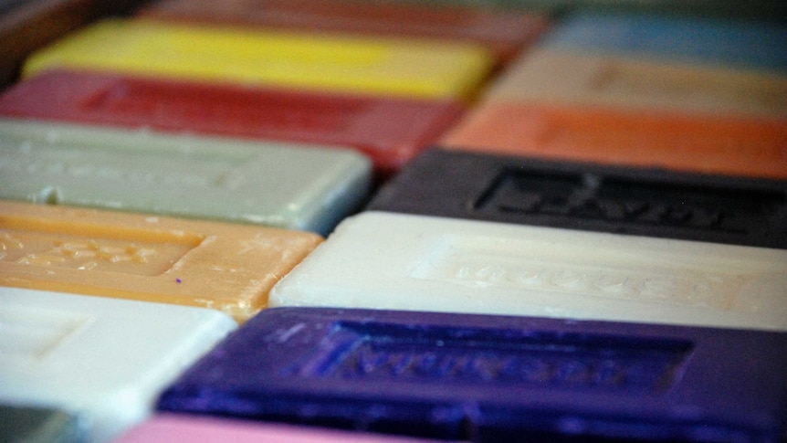 More than a dozen brightly coloured bars of soap lie in a row on a flat surface.