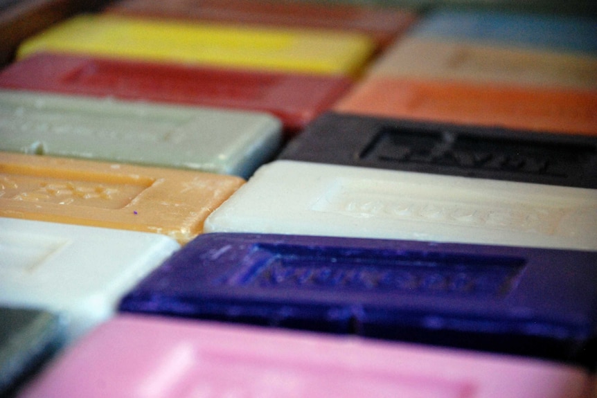 More than a dozen brightly coloured bars of soap lie in a row on a flat surface.