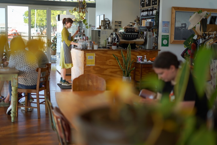 A woman stands at a counter at a cafe. In front of her is a girl sitting at a cafe table