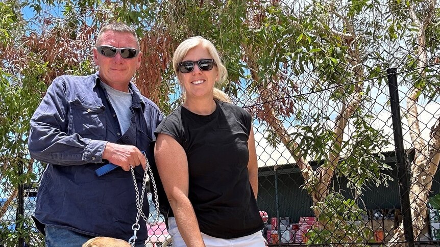Teacher Jodie Mackrell standing in front of a cyclone fence with husband Vince and two dogs
