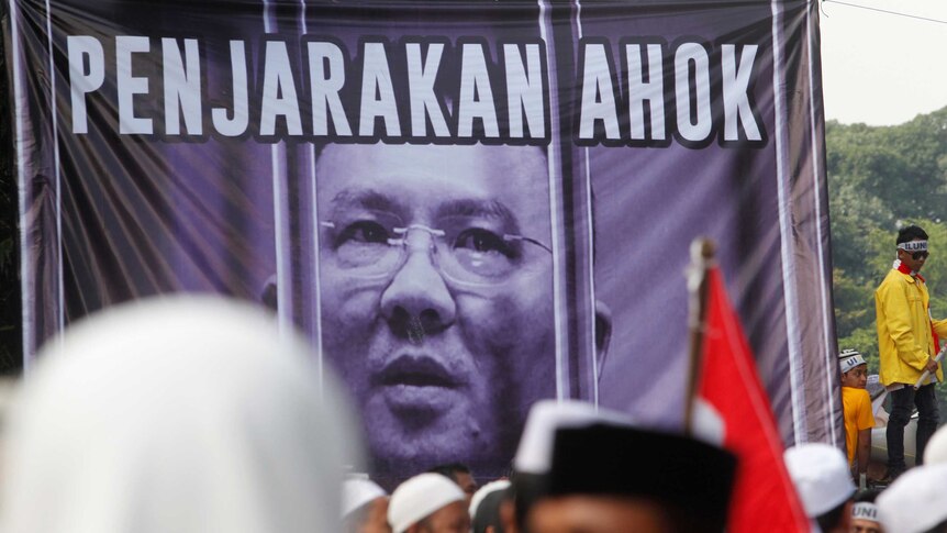 Hardline Muslim groups stand around a poster during protest against Jakarta's incumbent governor