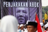Hardline Muslim groups stand around a poster during protest against Jakarta's incumbent governor