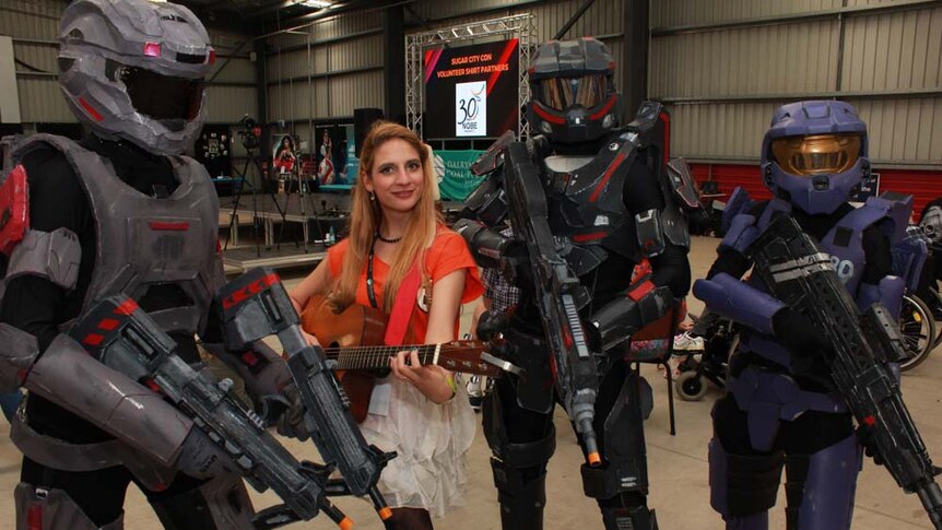 people in costume. Girl in the middle holding a guitar and smiling.