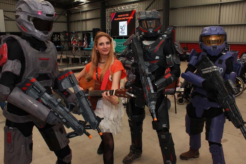 people in costume. Girl in the middle holding a guitar and smiling.