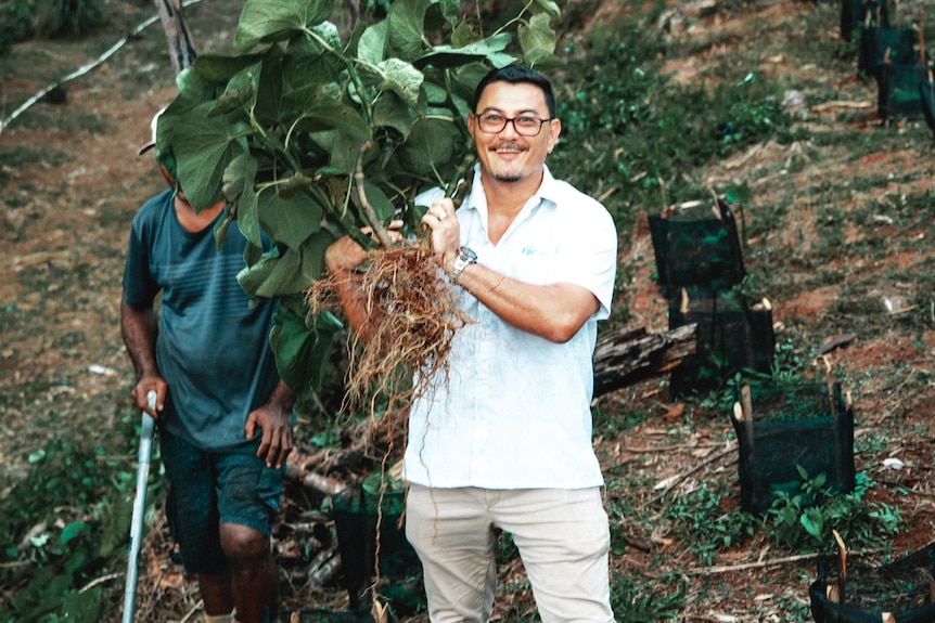 A middle-aged man with dark hair and glasses holding a root that appears to have just been pulled from the ground.