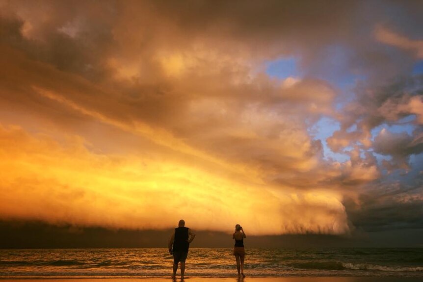 Two people stand looking at an enormous cloud rolling into Cable Beach.