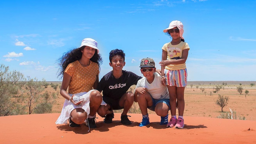 Four children pose for a photo on a red sand dune.