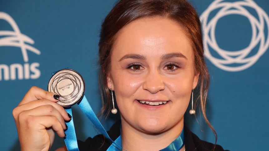 Ashleigh Barty smiles and holds up a medal.