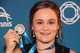 Ashleigh Barty smiles and holds up a medal.