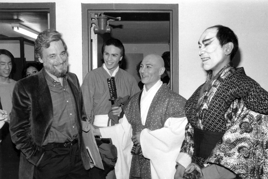 Stephen Sondheim stands smiling next to people dressed in traditional Japanese atire