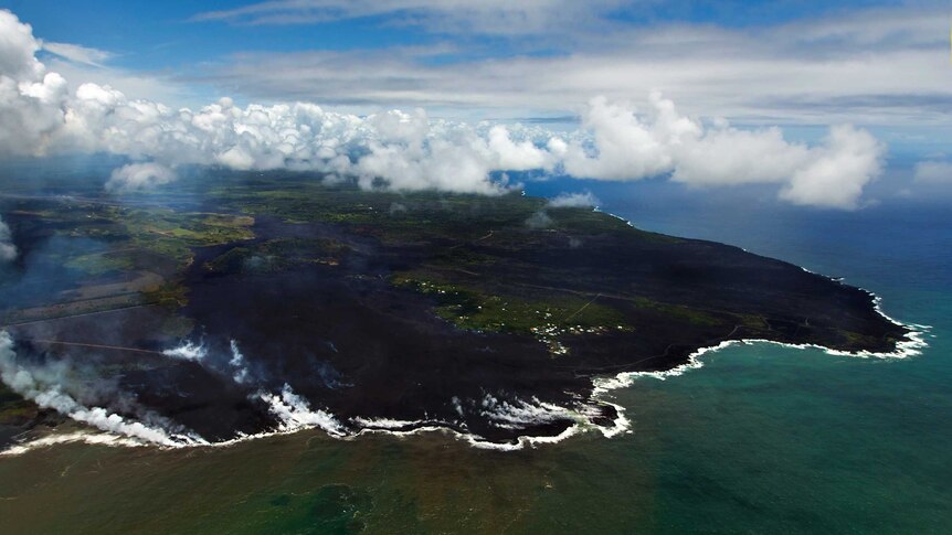 Steam rises as lava flows meet the ocean on Hawaii's coastline.