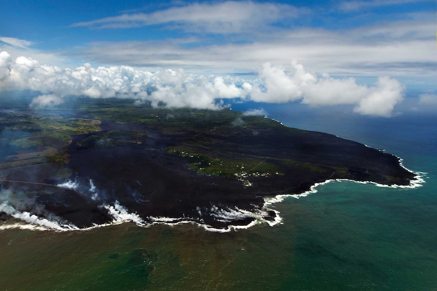 Steam rises as lava flows meet the ocean on Hawaii's coastline.