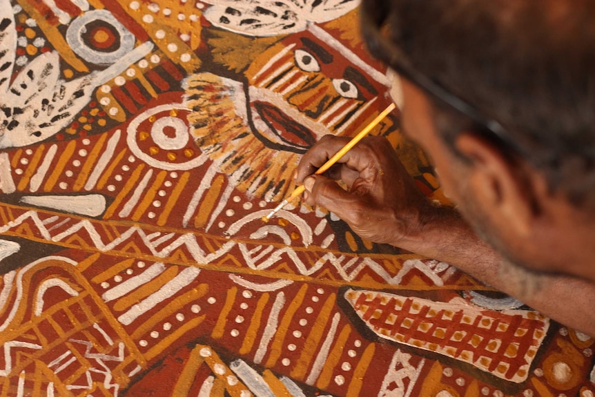 A man paints a huge artwork at Tiwi Arts in the Northern Territory.