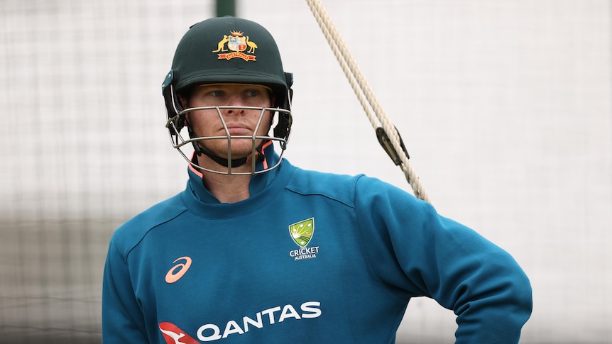 Australian cricketer Steve Smith looks serious as he stands wearing his helmet and a training top.   