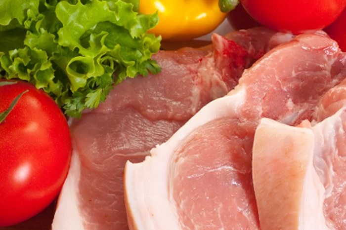 A close-up of raw pork steaks, with a tomato and lettuce in the background.