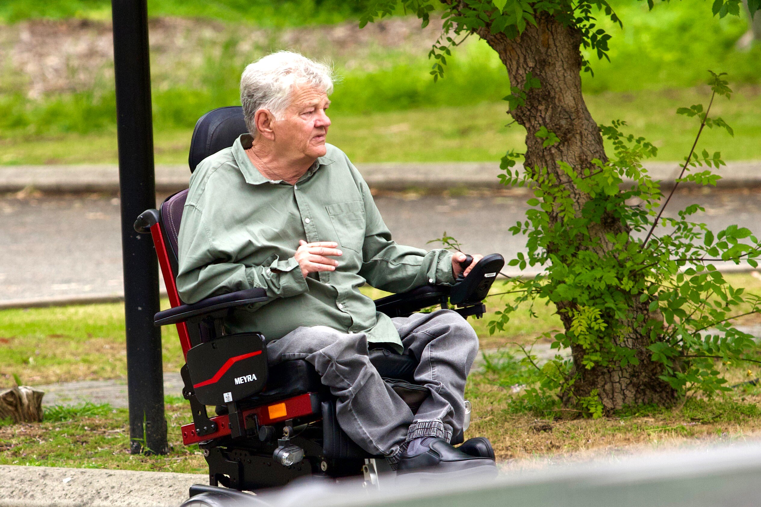 A man in an electric whelchair next to a tree.