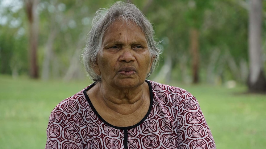 Stolen Generations NT Chairperson Eileen Cummings looks at the camera with lawn and trees in the background.