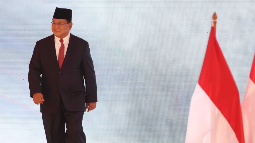 Indonesian presidential candidate Prabowo Subianto walks on the stage near flags.