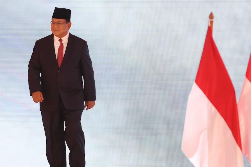 Indonesian presidential candidate Prabowo Subianto walks on the stage near flags.