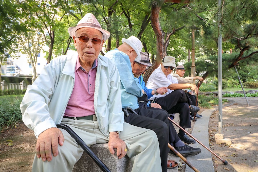 An elderly man in a short brimmed hat looks warmly towards the camera