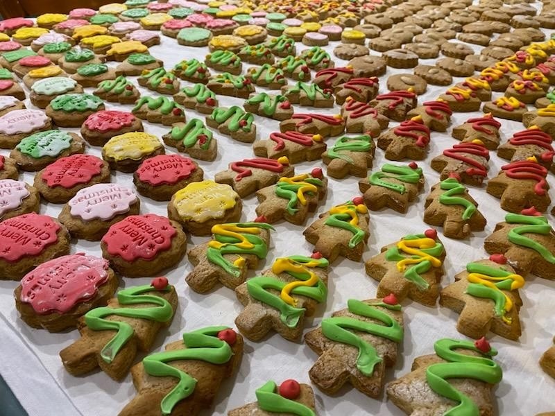 Sobre una mesa hay galletas decoradas en verde, rosa y verde. Hay cientos en forma de árboles y círculos. 