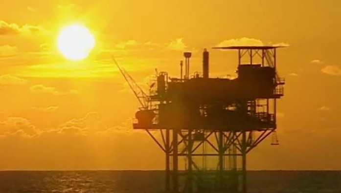 An oiil rig in the sea with a sunset in the background.