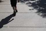 A generic shot of a child walking along a footpath. Only his legs and shadow are visible.