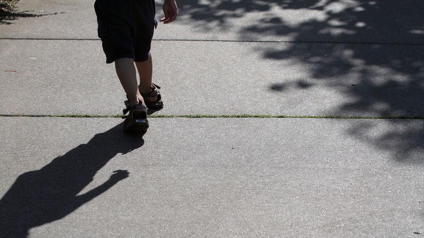 A child walks along a footpath, away from the camera, casting a shadow.