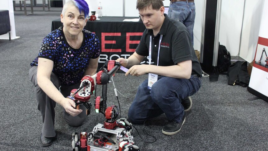 Woman with purple hair uses a robot with a pinching tool.