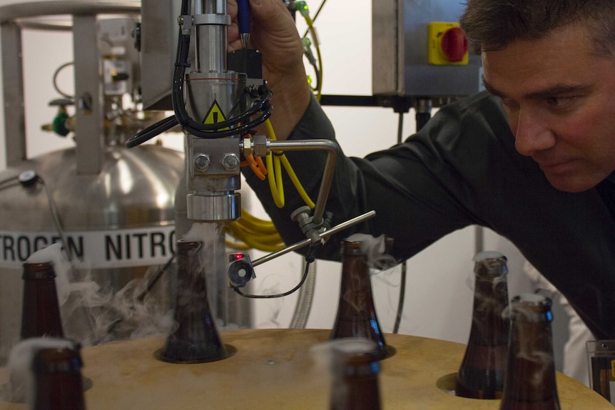 Man looks at a machine, white gas comes from beer bottles, sign in background says 'liquid nitrogen'
