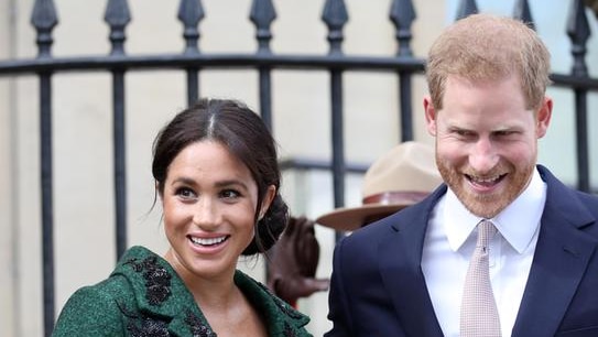 Meghan Markle holds a bouquet of flowers as she wears an emerald dress and coat, next to Prince Harry in a dark suit.